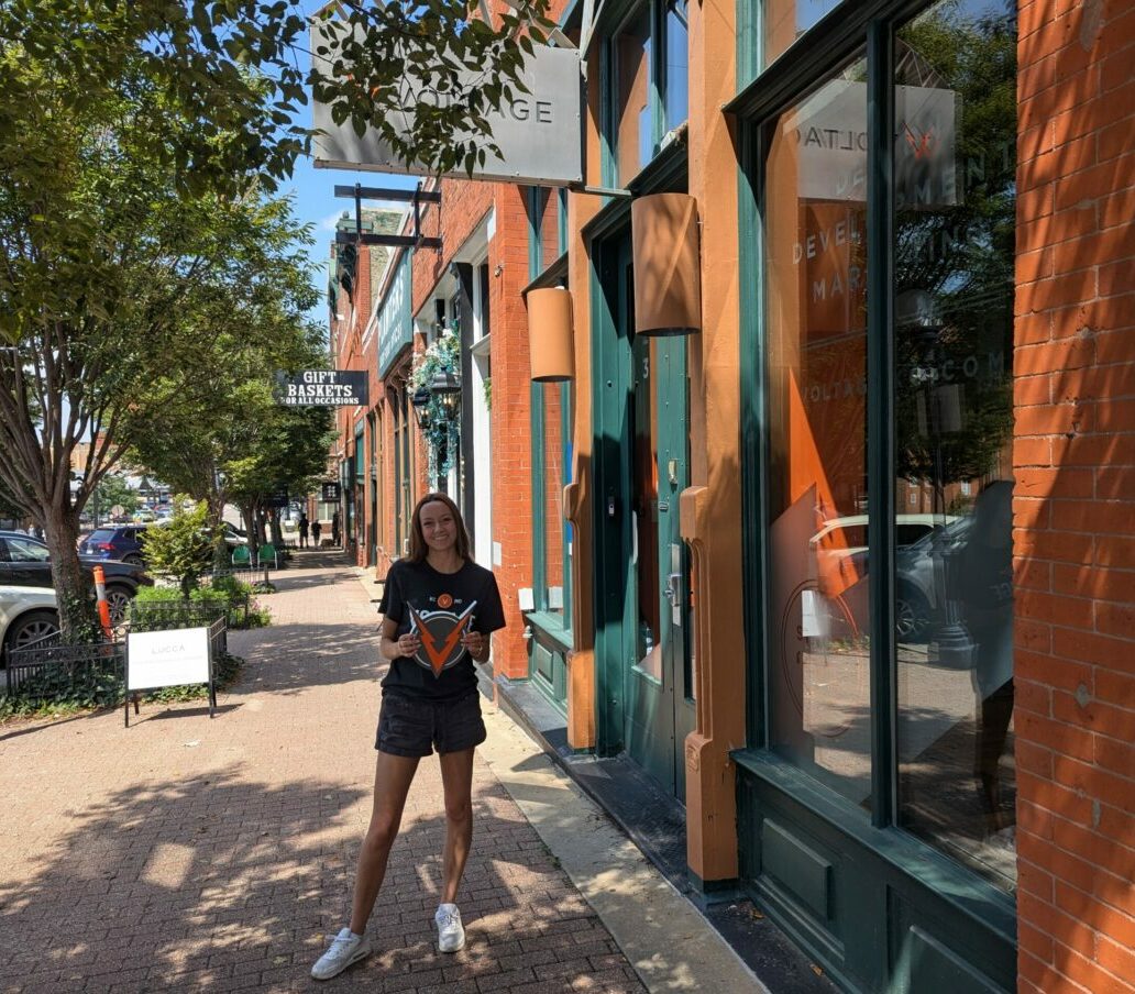 Intern Emily standing outside VOLTAGE building, holding VOLTAGE logo sign