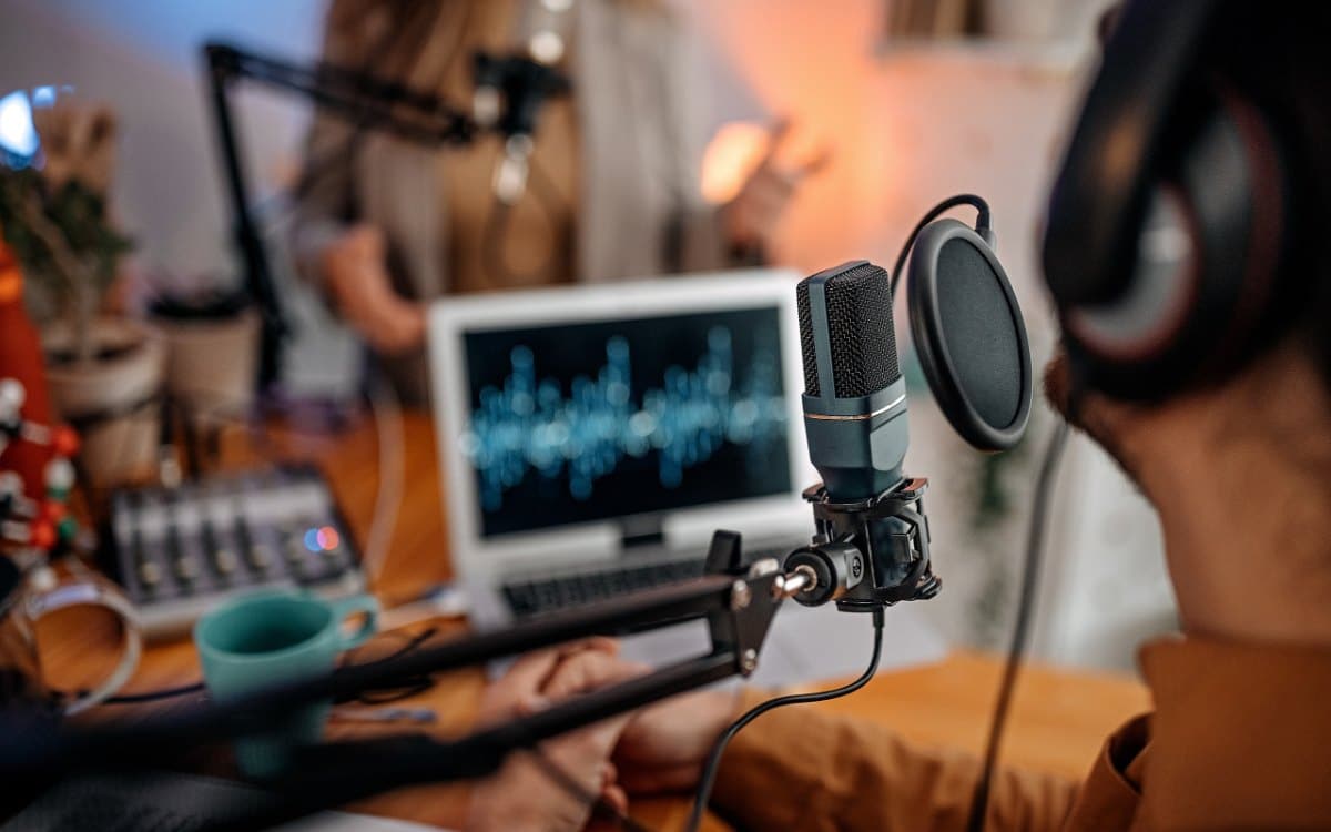 Podcast recording setup with a microphone, headphones, and a laptop showing an audio waveform.